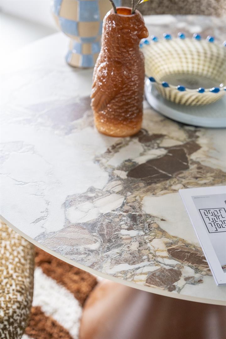 Ronde eettafel met een elegant tafelblad in marmerlook van gesinterde steen en een bruin, zandlopervormig metalen onderstel.
