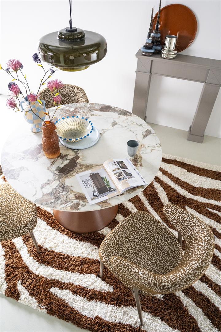 Ronde eettafel met een elegant tafelblad in marmerlook van gesinterde steen en een bruin, zandlopervormig metalen onderstel.